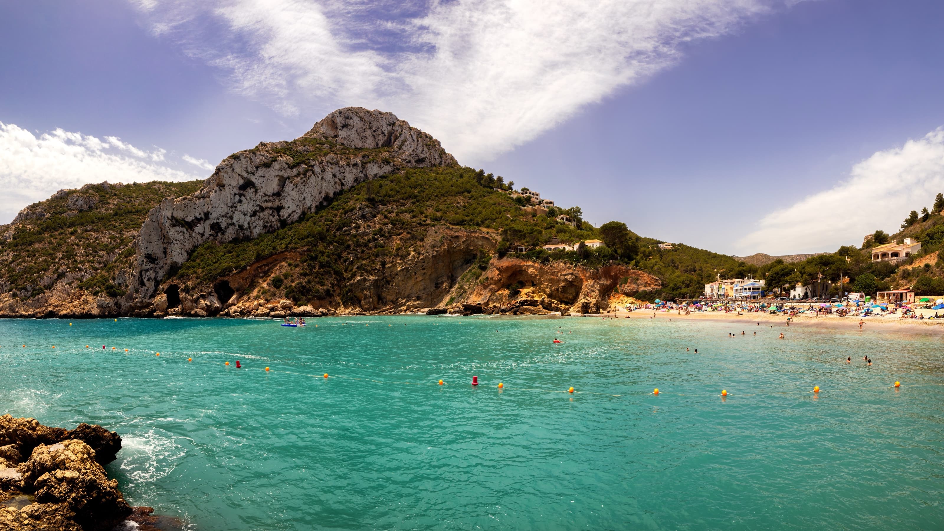 Panorama de la cala de la Granadella en été : eau turquoise, plage de galets et falaises couvertes de pins