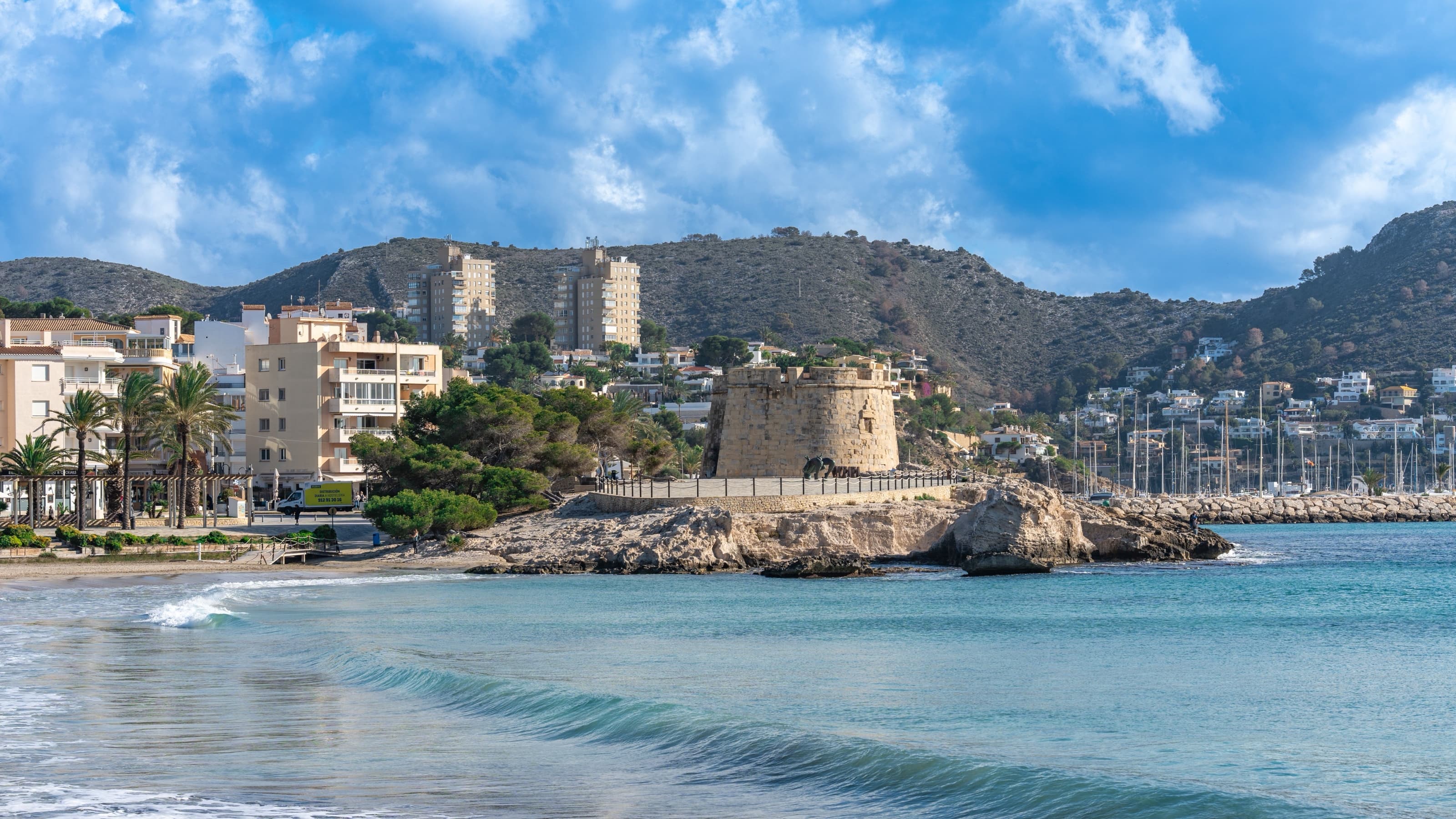 La plage de l’Ampolla à Moraira, avec le château circulaire du XVIIIe siècle et les mâts du port derrière