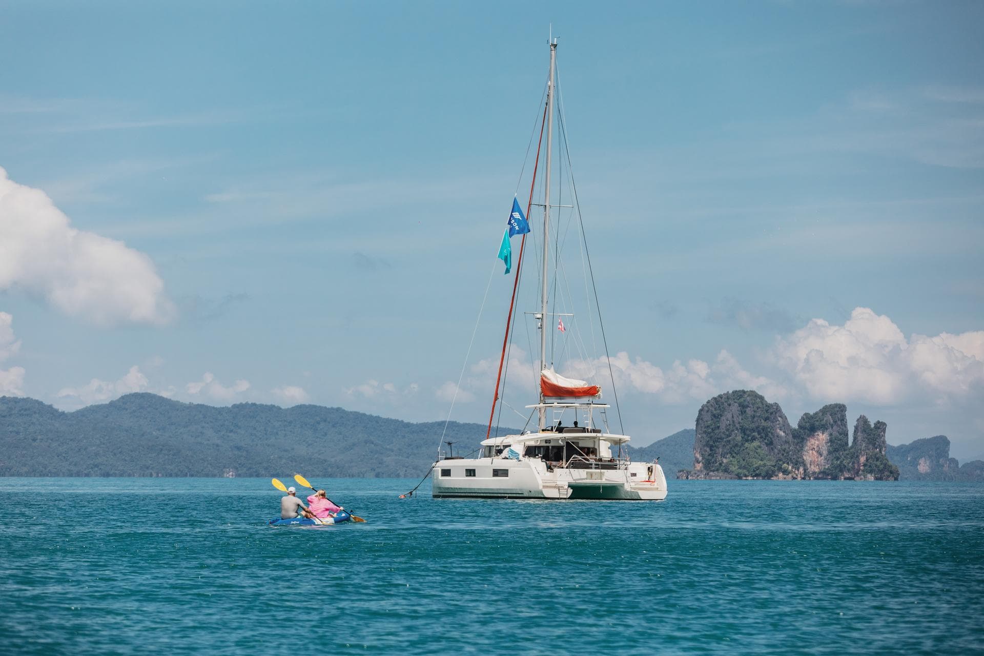 Deux personnes en kayak rejoignent un catamaran Lagoon au mouillage dans une baie calme